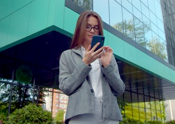 Businesswoman in suit using a smartphone outdoors near a modern office building.