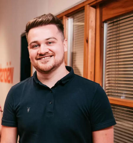 Smiling man in a dark polo shirt standing in front of a door.